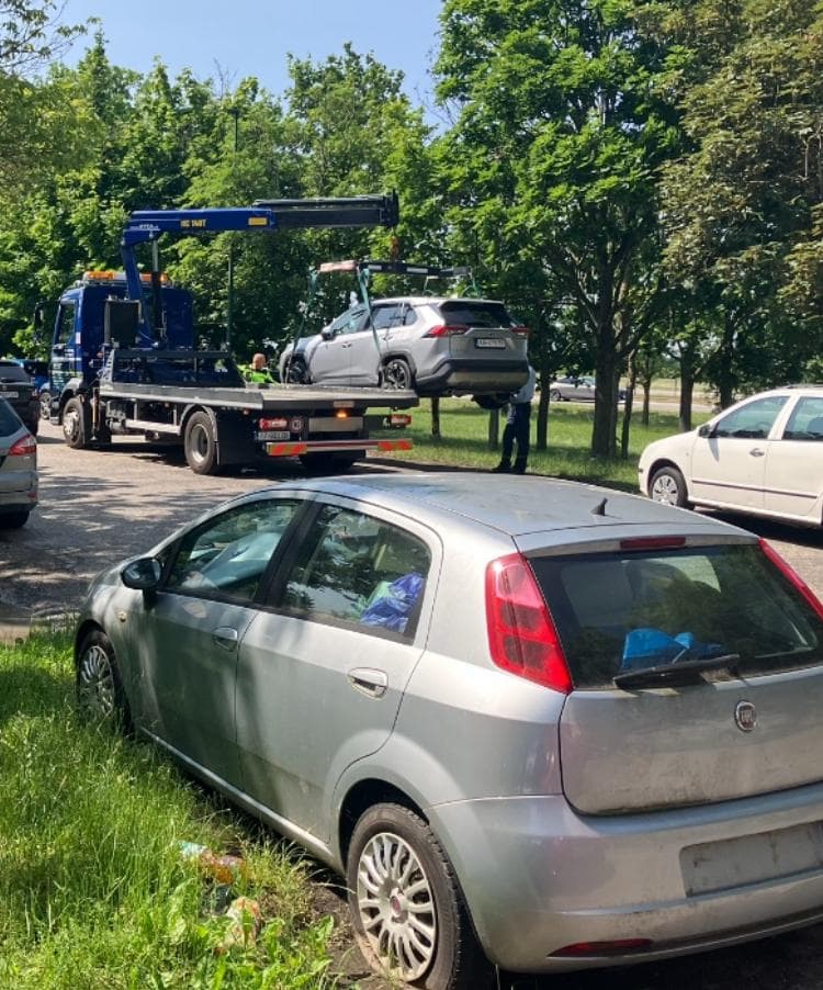 Dlhodobo opustený a neriešený vrak, v pozadí mestská odťahovka prekladajúca vozidlo. Foto: Redakcia Marker