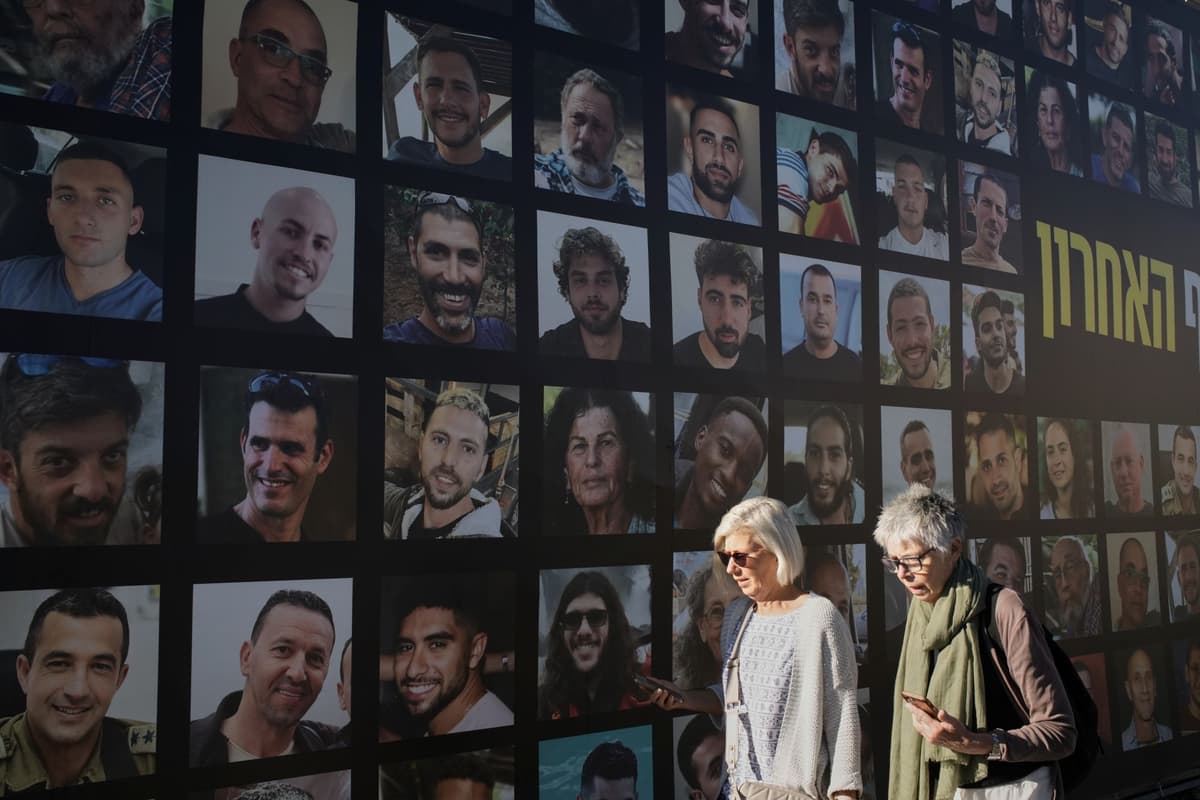 Ženy prechádzajú okolo transparentu s fotografiami rukojemníkov, ktorých uniesol a zadržiaval Hamas v Pásme Gazy, v Jeruzaleme, v utorok 7. októbra 2025. Foto: TASR/AP